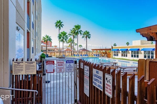 A pool area with palm trees, a wooden fence, and signs indicating private property and no luggage carts.