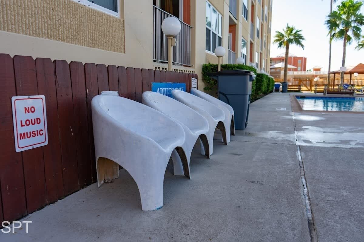 Outdoor seating with a 'No Loud Music' sign, a pool, and a building with balconies.