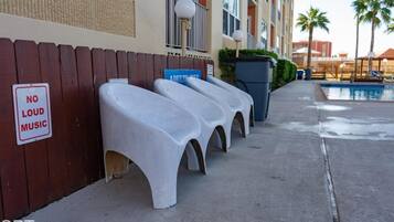 Outdoor seating with a 'No Loud Music' sign, a pool, and a building with balconies.