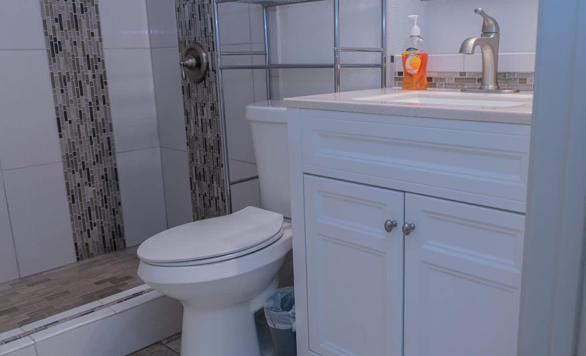 A bathroom with a white toilet, a shower with a tiled wall, and a sink with a soap dispenser.