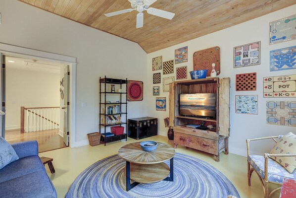 Una sala de estar acogedora con techo de madera, una estantería, un televisor y varios juegos de mesa en las paredes.