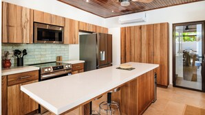 A modern kitchen with wooden cabinets, stainless steel appliances, a large island, and a ceiling fan.