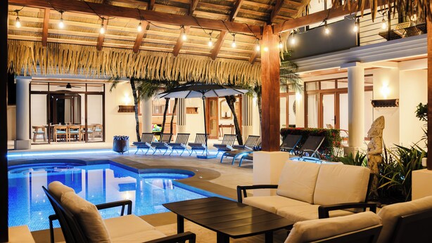 A pool area with lounge chairs, a table, and a ceiling with exposed beams and string lights.