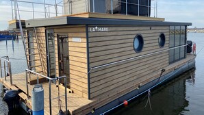 Een drijvend woonschip met een houten dek, een overdekt bovenbdek en een naamplaatje met de tekst 'LA MARE'.