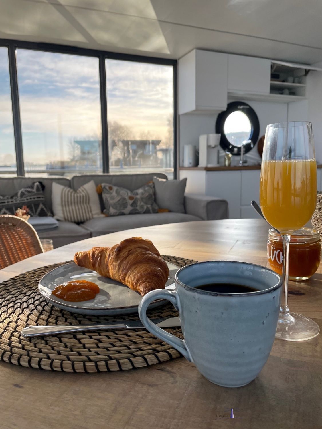 A breakfast setting with croissants, coffee, and orange juice on a table with a view of the city through large windows.