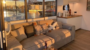 Een moderne woonkamer met een bank, een koffieapparaat en uitzicht op een gracht.