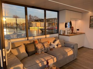 A modern living room with a sofa, a coffee machine, and a view of a canal.