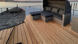Een houten terras met een overdekte zithoek en uitzicht op het water.