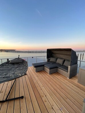 A wooden deck with a covered outdoor seating area and a view of the water.