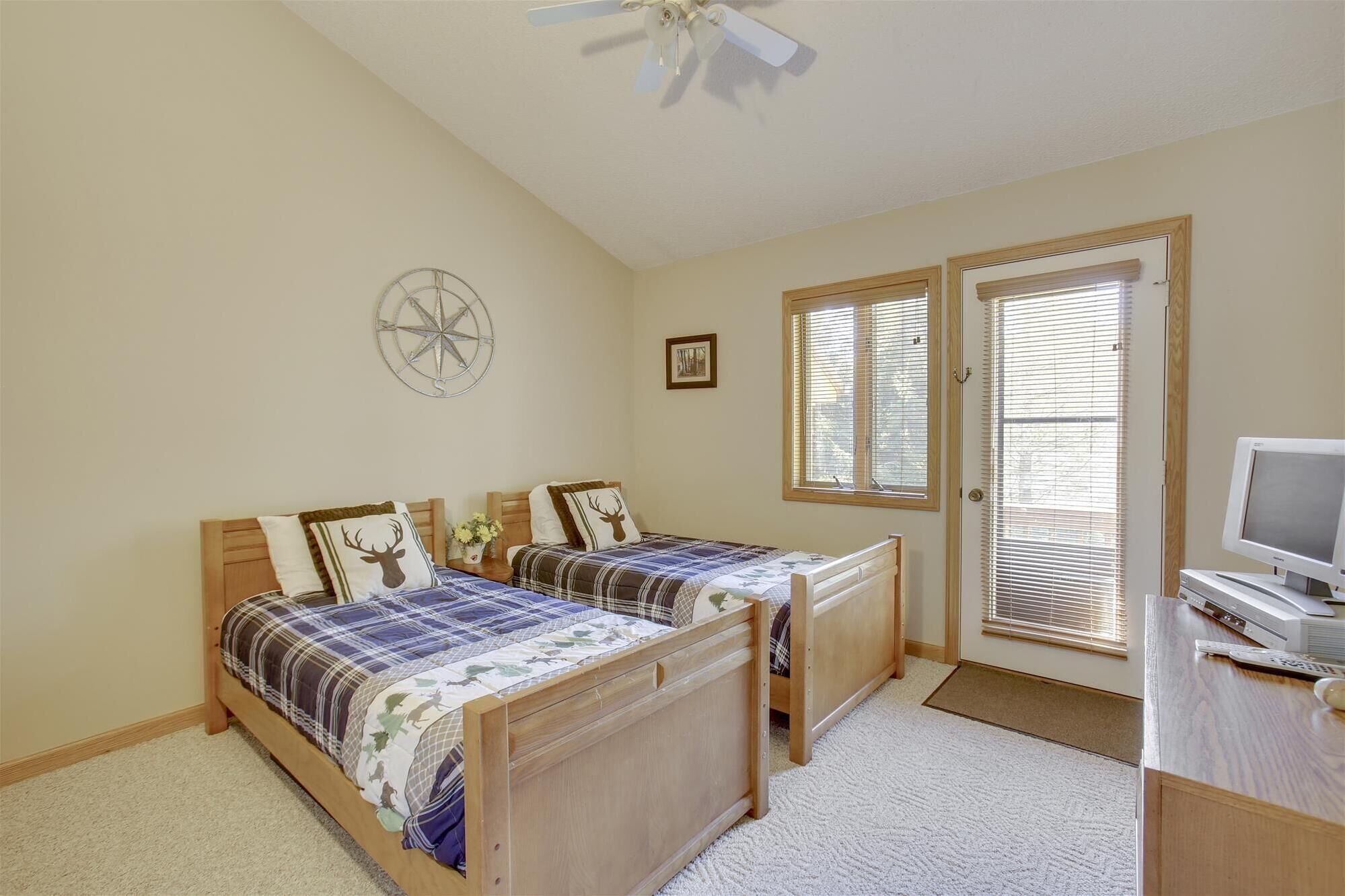 A bedroom with two wooden beds, a ceiling fan, a compass wall decoration, a framed picture, and a desk with a computer and printer.