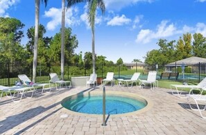 Una piscina circular con barandilla de seguridad metálica, rodeada de sillas reclinables blancas y un patio de ladrillo.
