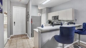 A modern kitchen with white cabinets, a central island with bar stools, and a refrigerator. - Luxury n cozy 3 bed 2 bath vacation property in a gated community (Kissimmee)