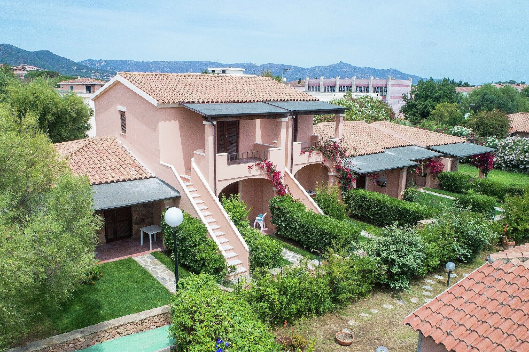 Ein Wohnhaus mit Ziegeldach, einer überdachten Terrasse und einem gepflegten Garten mit Hecken und einem kleinen Teich.