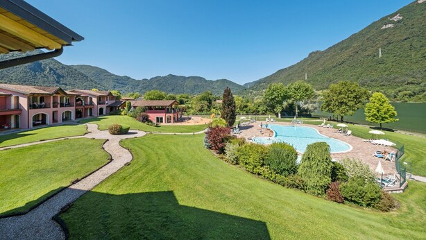A hotel with a swimming pool, green lawns, and mountains in the background. - Apartment by Lake Idro with Mountain Views (Idro (bs))