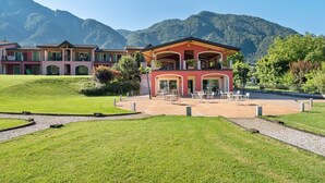 A hotel with a central building and two wings, surrounded by a well-maintained lawn and a gravel path. - Apartment by Lake Idro with Mountain Views (Idro (bs))
