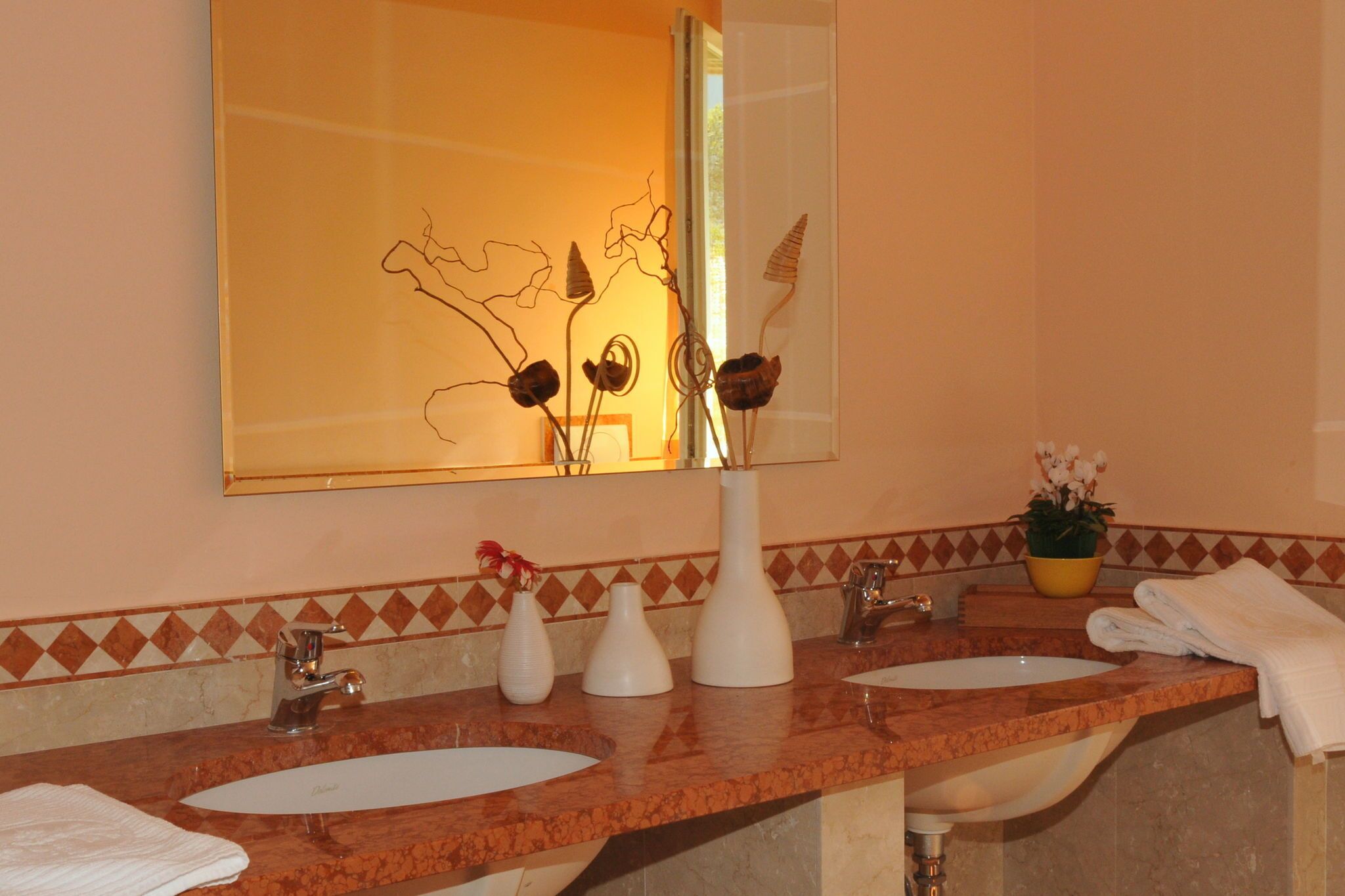A bathroom with two sinks, a large mirror, and decorative vases.