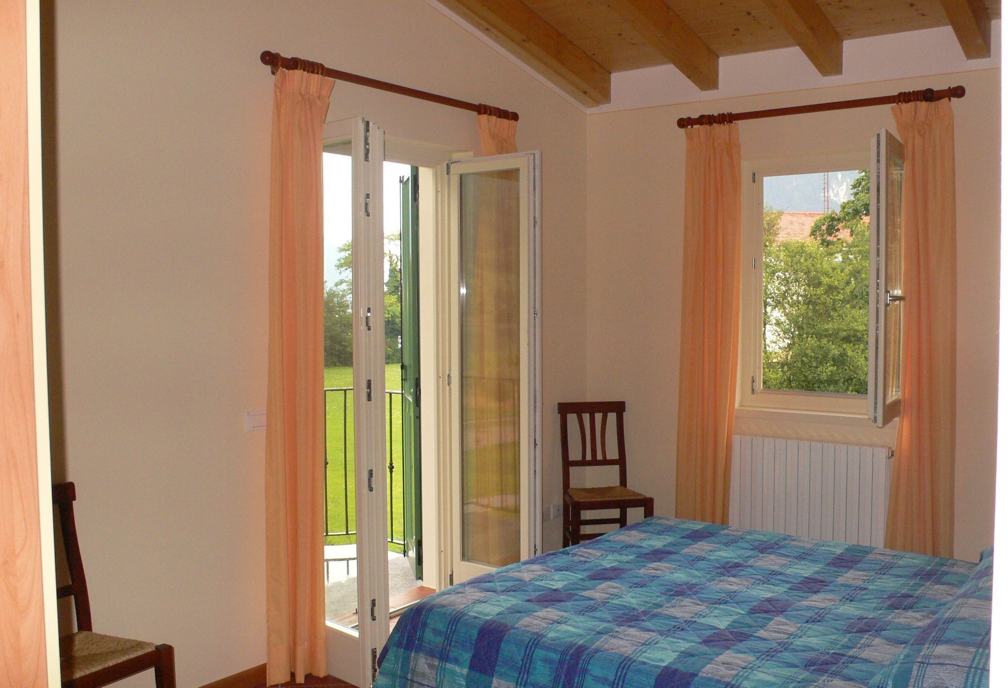 A bedroom with a bed, a chair, a window with curtains, and a door leading to a balcony.