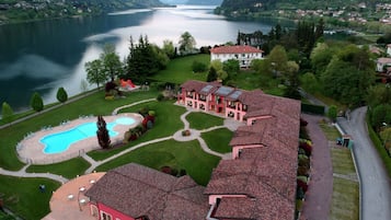 Una amplia villa con piscina, cancha de tenis y vistas a un lago rodeado de montañas.