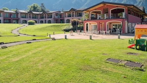 A hotel with multiple buildings, a central patio area with outdoor seating, and a playground. - Apartment on Lake Idro with Pool (Idro (bs))