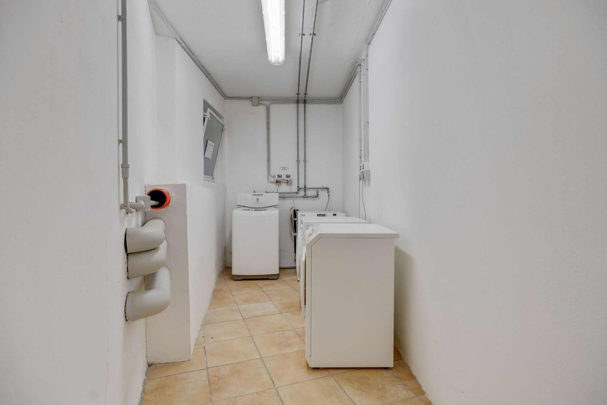Un cuarto de lavandería con paredes blancas, piso de baldosas y una hilera de lavadoras.