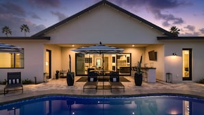A modern house with a swimming pool, outdoor seating, and a well-lit patio area.