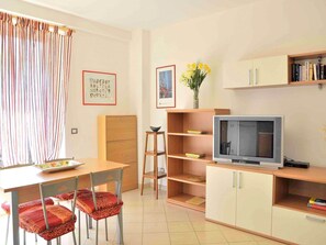 Una habitación con una mesa de comedor, sillas, un televisor, una estantería y un ventanal con cortinas.