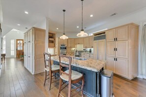 A spacious kitchen with wooden cabinets, a granite countertop island, and pendant lighting.