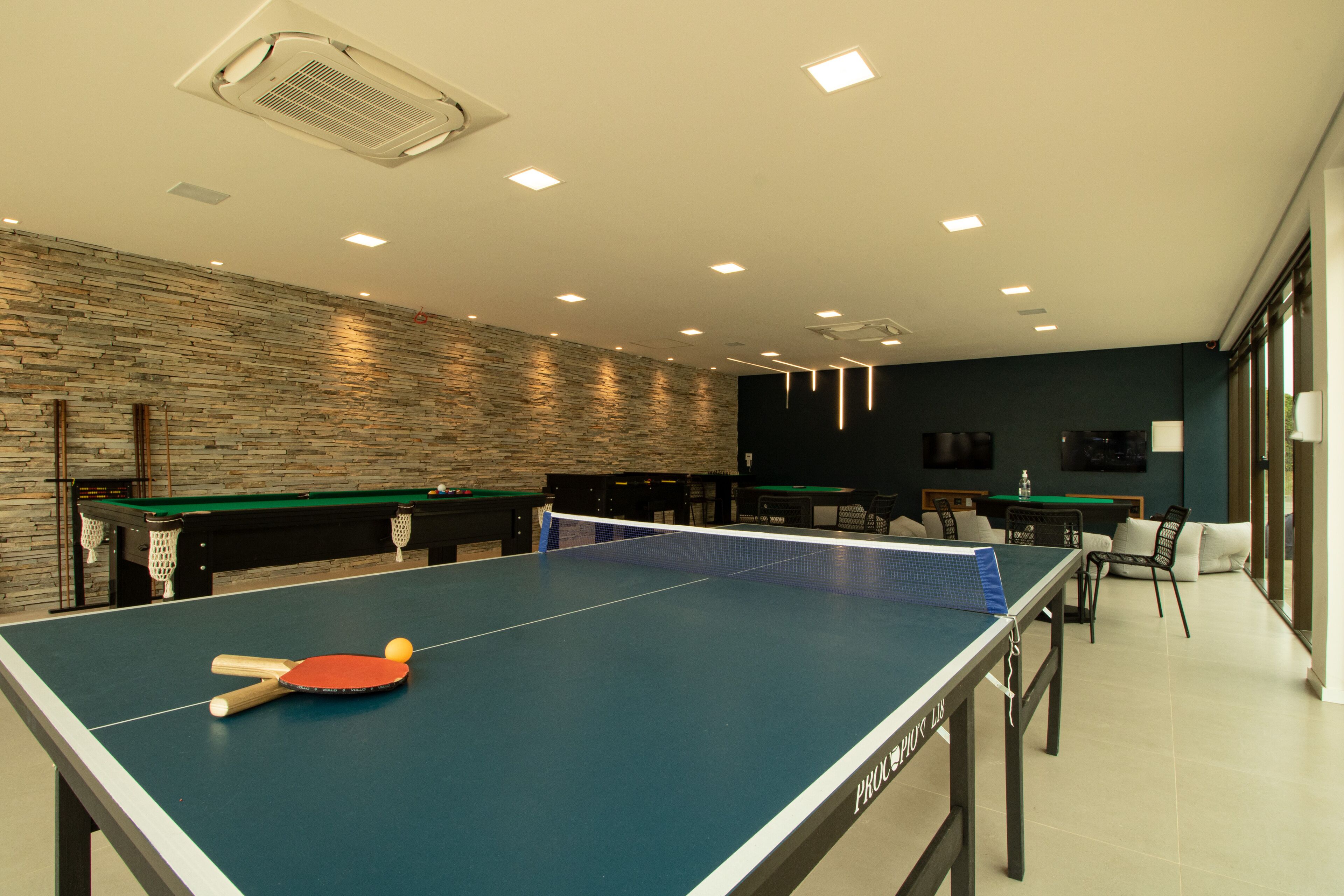 Un tavolo da ping pong con racchette e pallina, un tavolo da biliardo e un'area bar con sedie e televisore.