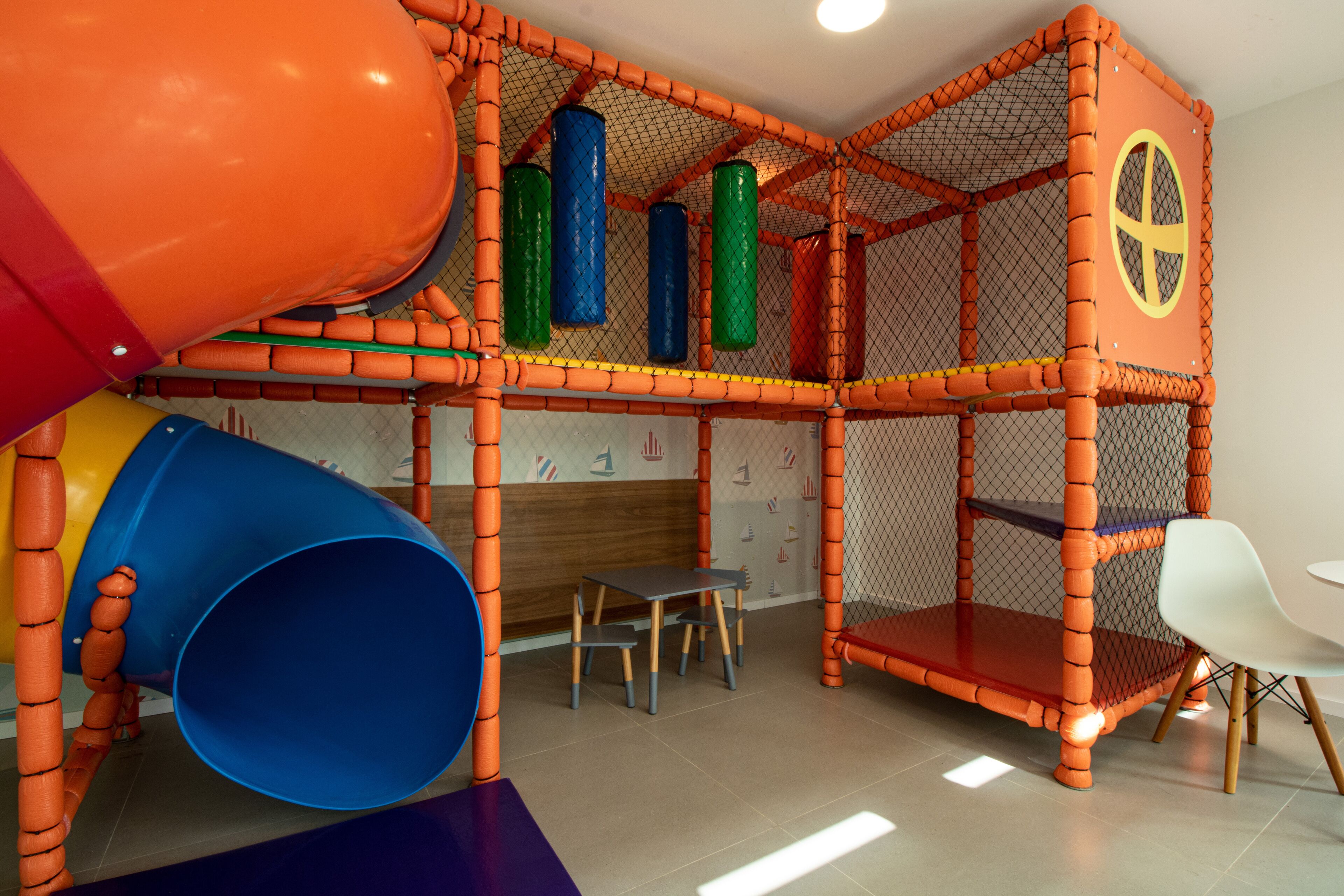 A play area with a slide, a climbing net, and a table with chairs.