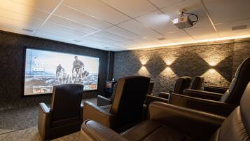 Un cine en casa con sillones de cuero reclinables, una pantalla grande y un proyector.