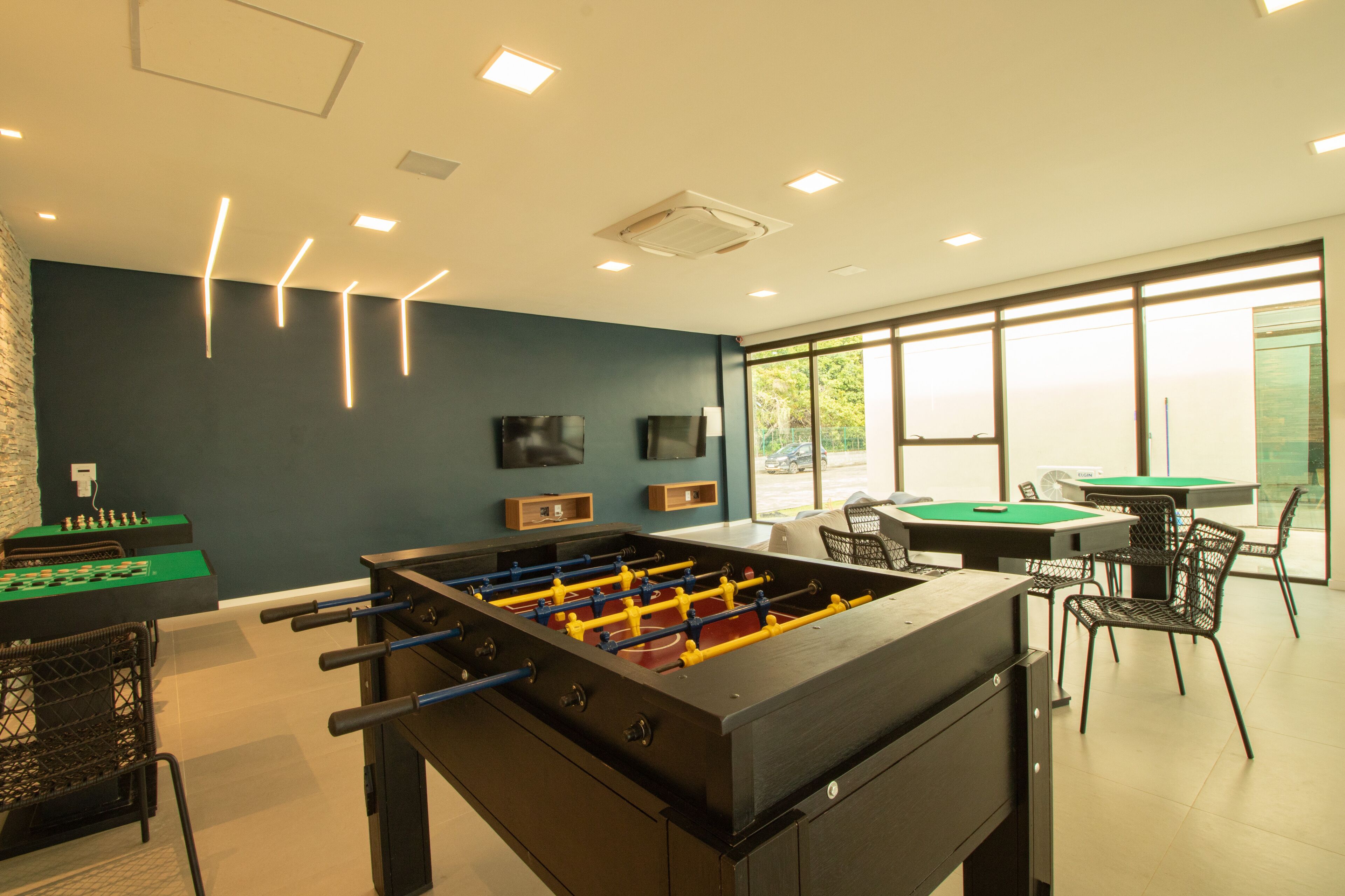 Una habitación con mesa de fútbol, mesa de billar y zona de bar con sillas.