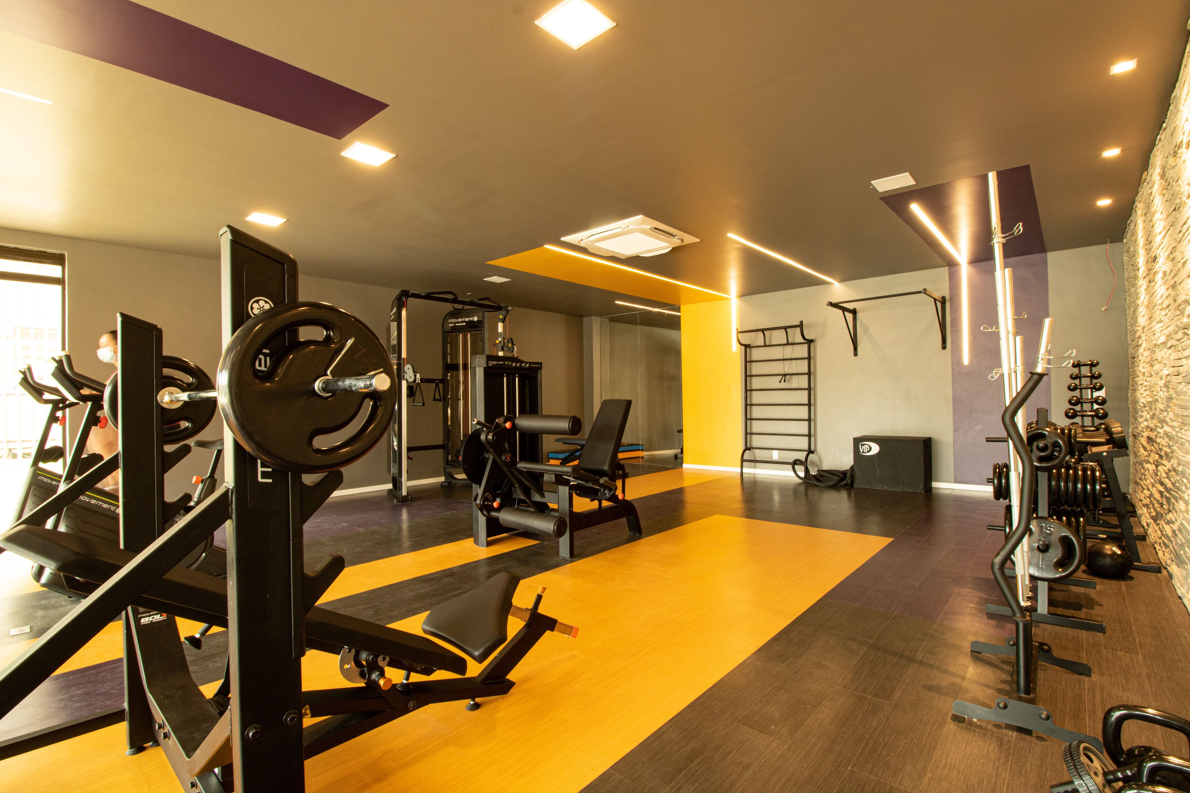 Een sportschool met diverse trainingsapparaten, een halterbank en een pull-up bar aan de muur.