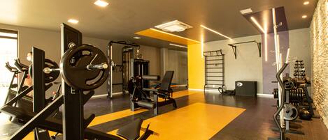 Een sportschool met diverse trainingsapparaten, een halterbank en een pull-up bar aan de muur.