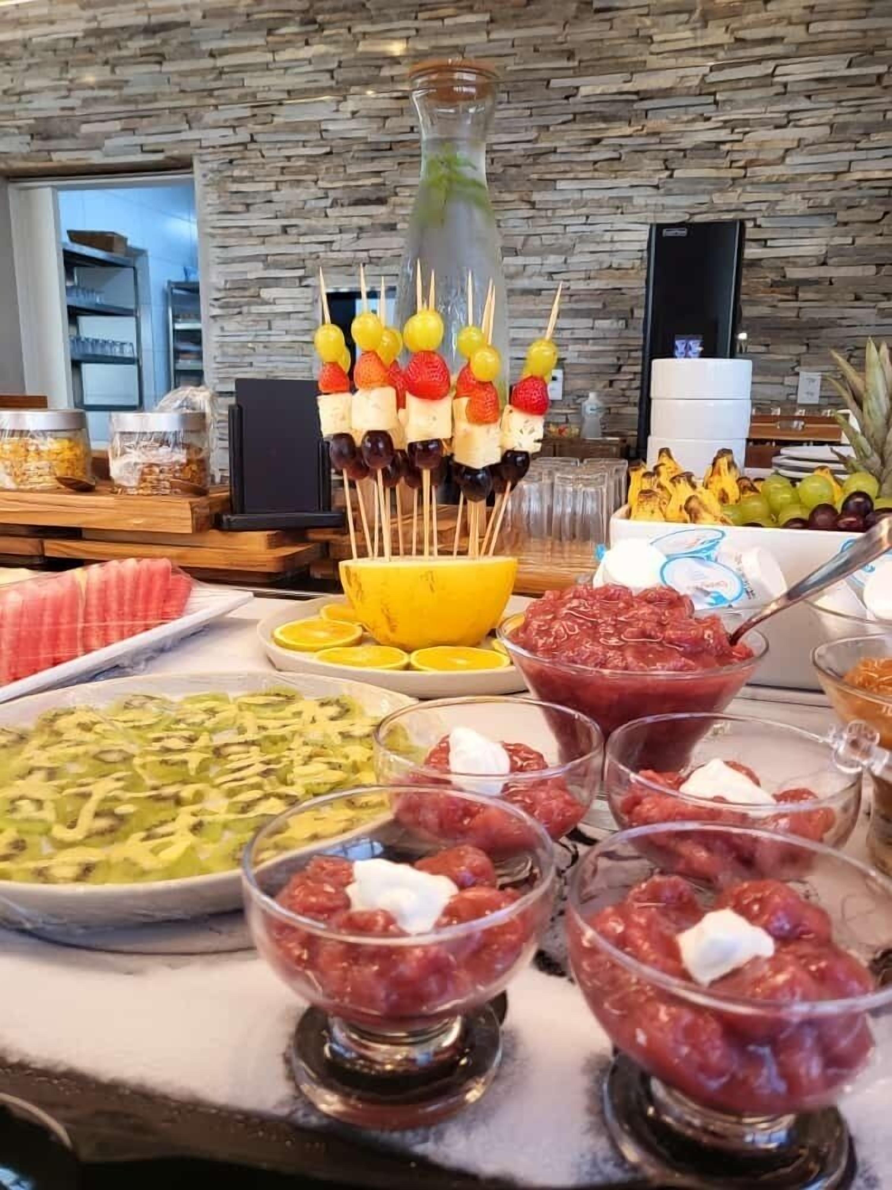 Un bufé con diversas opciones de comida, como brochetas de fruta, un tazón de fruta y tazones con salsas.