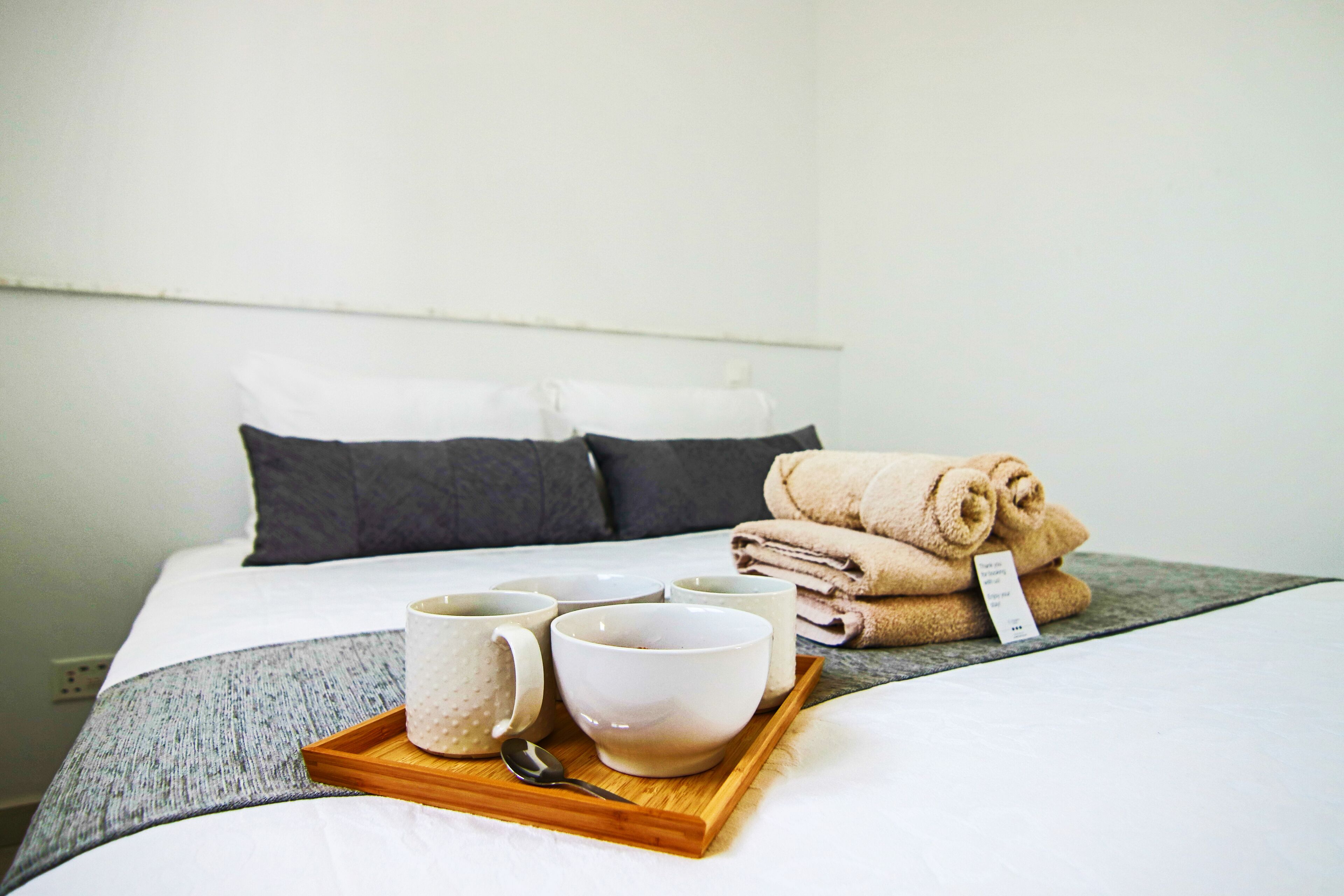 Una cama bien tendida con almohadas, una bandeja con tazas y un bol, y toallas enrolladas.