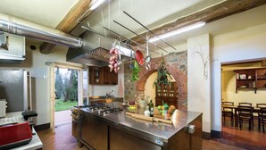 A kitchen with a large island, stainless steel appliances, hanging pots, and a brick wall.