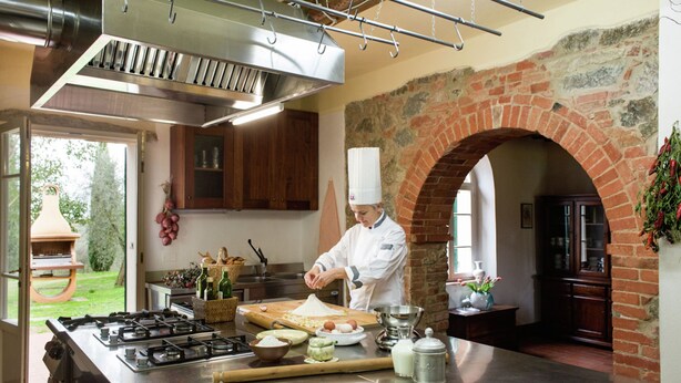 A chef preparing food in a kitchen with a large island, brick archway, and wooden cabinets.