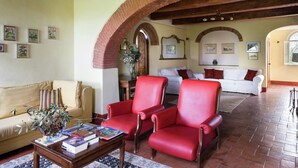 A spacious living room with a brick archway, a beige sofa, red armchairs, and a coffee table with books.