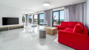 Ein modernes Wohnzimmer mit großem Fernseher, einem roten Sofa und Blick auf den Strand.