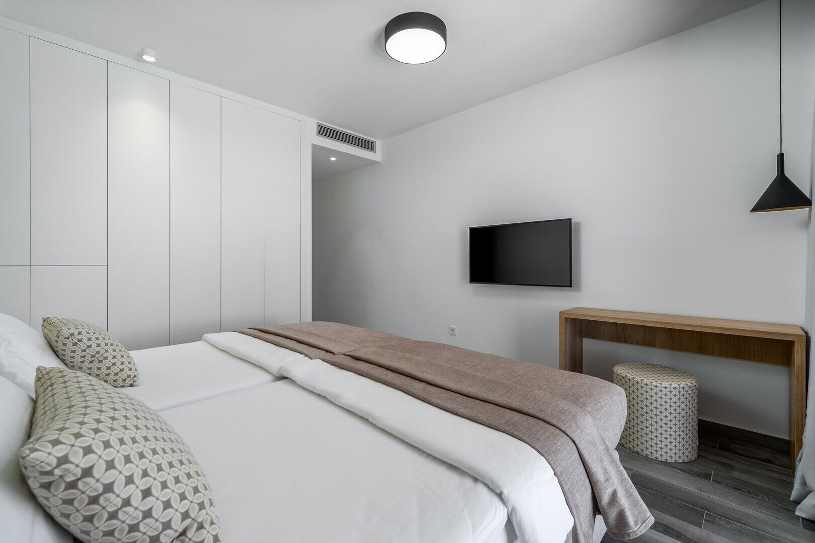 A modern bedroom with a bed, bedside tables, a TV, and a bench.
