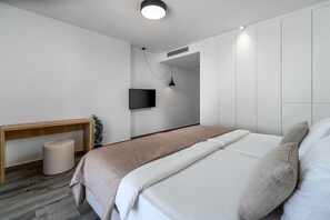Une chambre à coucher moderne avec un grand lit, un téléviseur fixé au mur et un banc en bois.