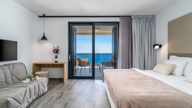 Ein modernes Hotelzimmer mit Bett, Sofa, Schreibtisch und einem Balkon mit Meerblick.