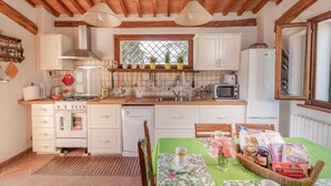 A kitchen with wooden beams, white cabinets, a window, and a dining table set with a basket of groceries.