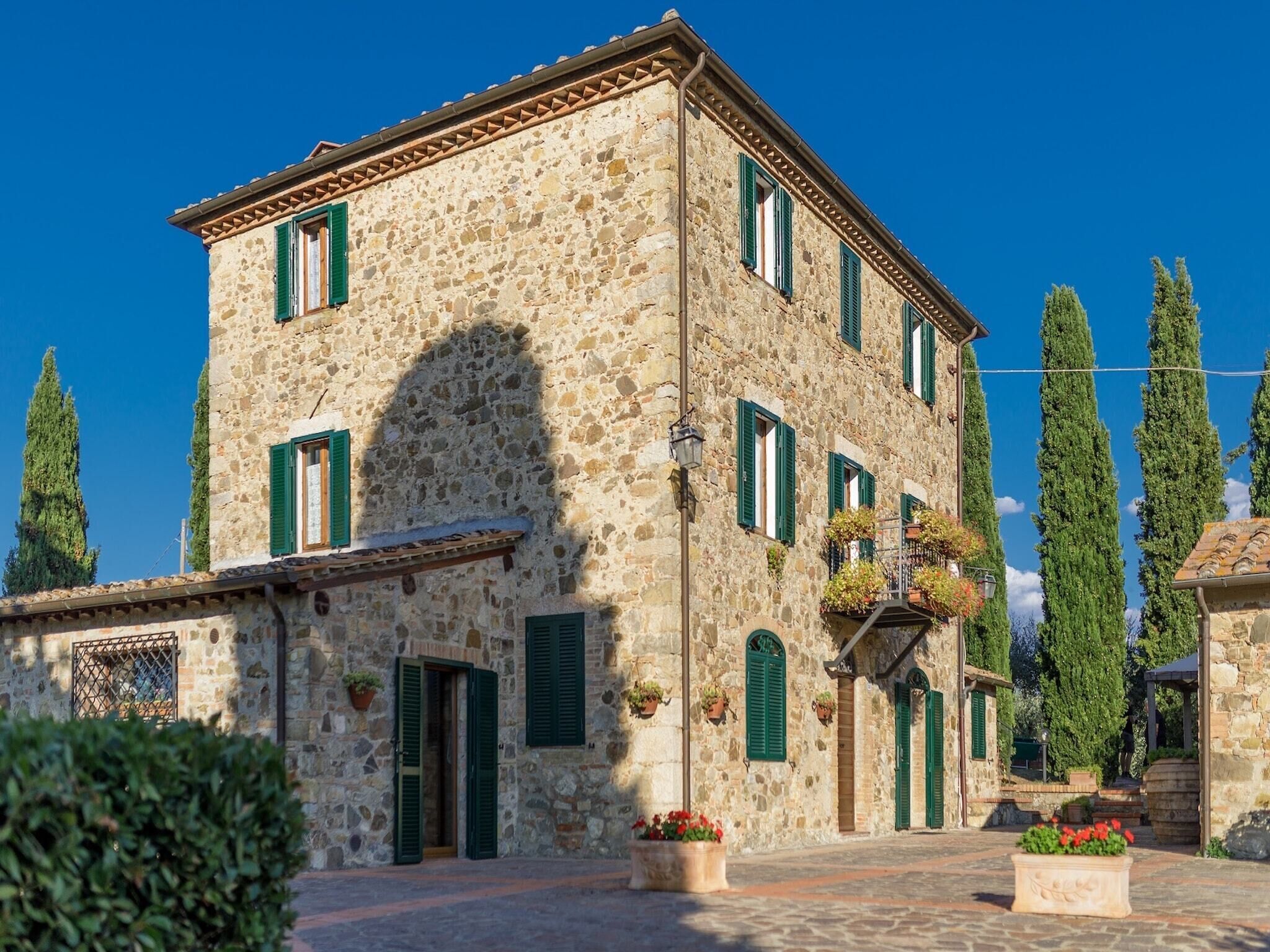 A stone building with green shutters, a courtyard, and tall trees.