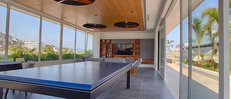 A spacious room with a ping pong table, large windows, and a ceiling fan.
