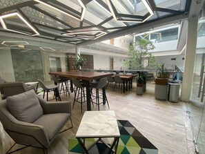 A modern interior with a high ceiling, a central wooden table surrounded by chairs, and a glass partition.
