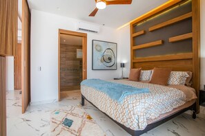 Un dormitorio con cama, ventilador de techo, equipo de aire acondicionado, un cuadro y alfombra estampada.