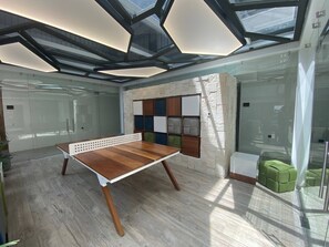 Una habitación moderna con mesa de ping pong, pared decorada con piedra y separador de vidrio.