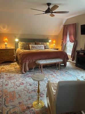 A bedroom with a bed, bedside lamps, a ceiling fan, a bench, and a patterned rug.