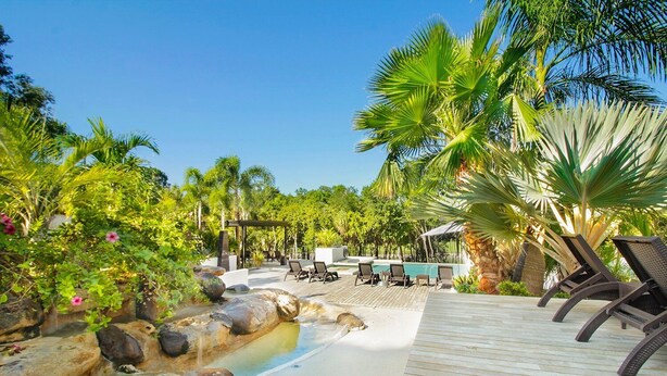 Un espace aménagé au bord de la piscine, avec des chaises longues, une terrasse en bois et une petite cascade.